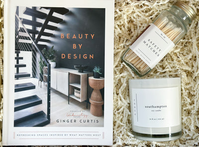 Looking for a thoughtful home décor gift?  Look no further than our "Luxury Living" Book, Candle, and Matches Coffee Table Gift Set! This exquisite package includes a stunning hardcover book by Ginger Curtis, titled "Beauty by Design", your favorite Southampton scent Roote soy candle, and a trendy glass jar filled with stylish safety matches.