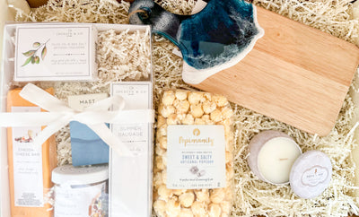 This Gift Set is the perfect way to show your appreciation. Whether it’s for a closing gift, housewarming, Corporate or simply just to say “thank you”, this carefully curated set has something for everyone. The small board is beautifully decorated with ocean blue colored resin art. In the perfectly wrapped white gift box with a clear lid, includes an assortment of delicious snacks, including mini organic chocolate, mini crackers, summer sausage, mixed nuts, and cheddar cheese. 